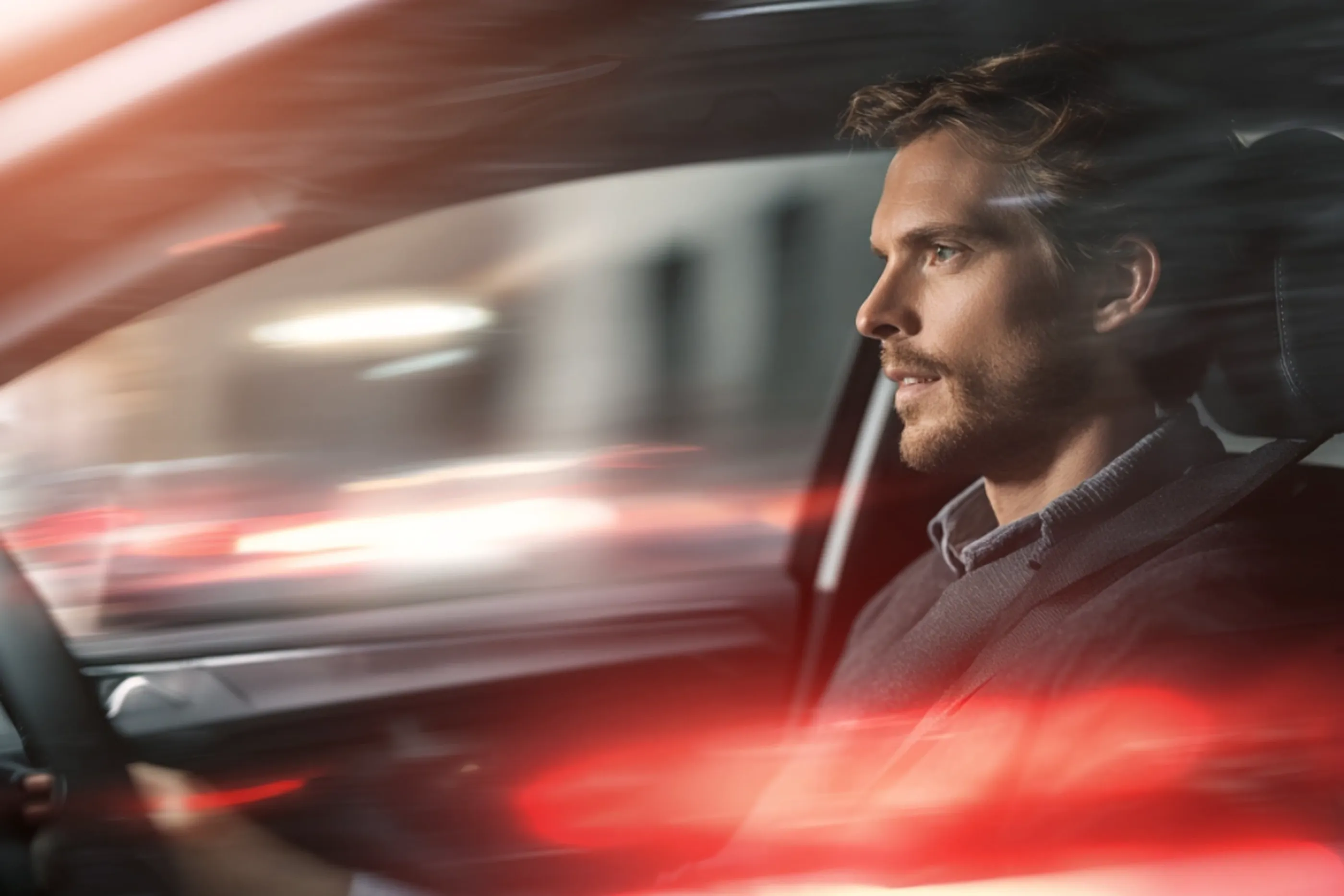 Mann fährt konzentriert ein Auto bei Nacht, Lichter der Stadt verschwimmen im Hintergrund.