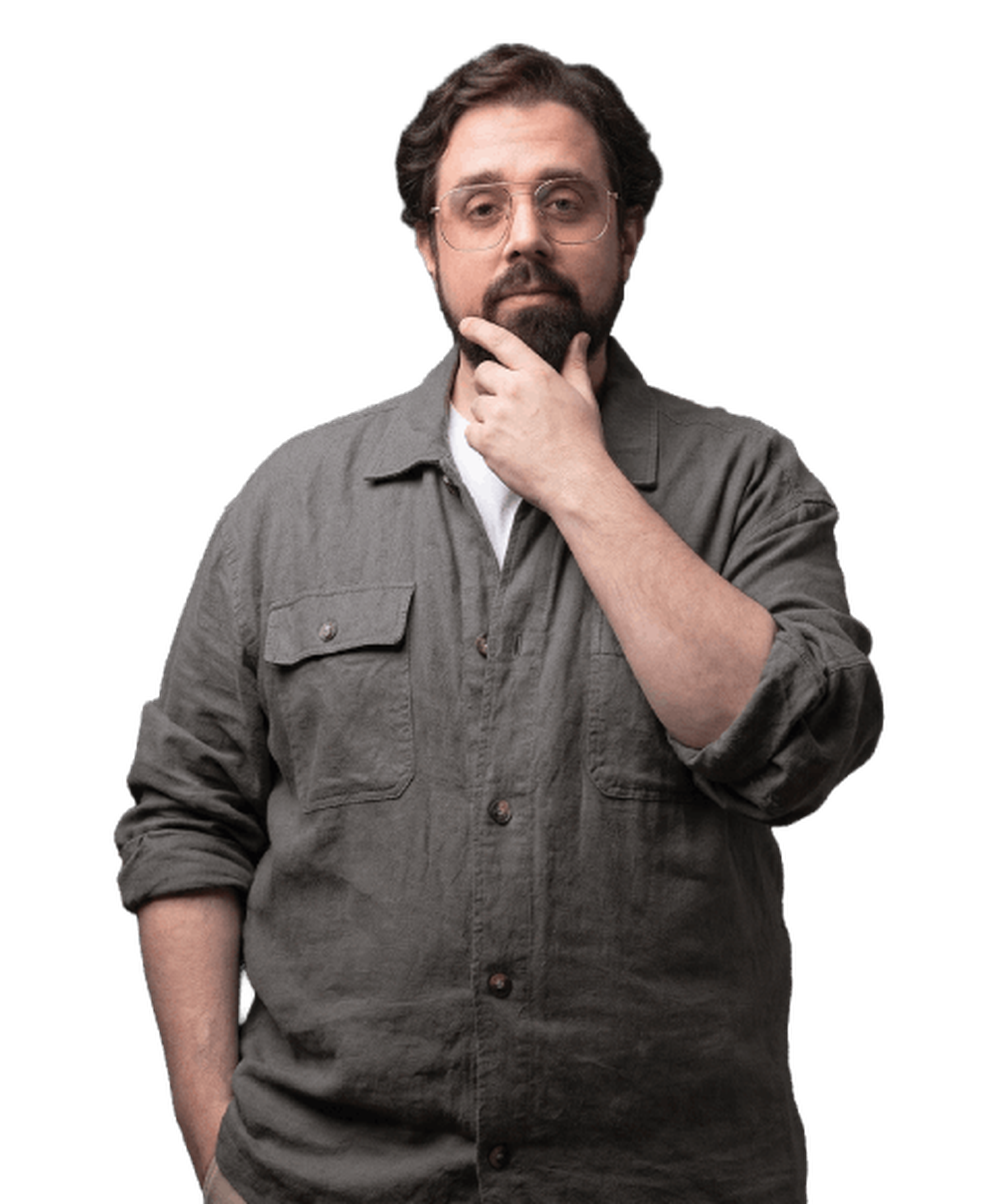 Man with glasses and beard stands against a black background, hand on chin in a thoughtful pose, wearing a gray button-up shirt.