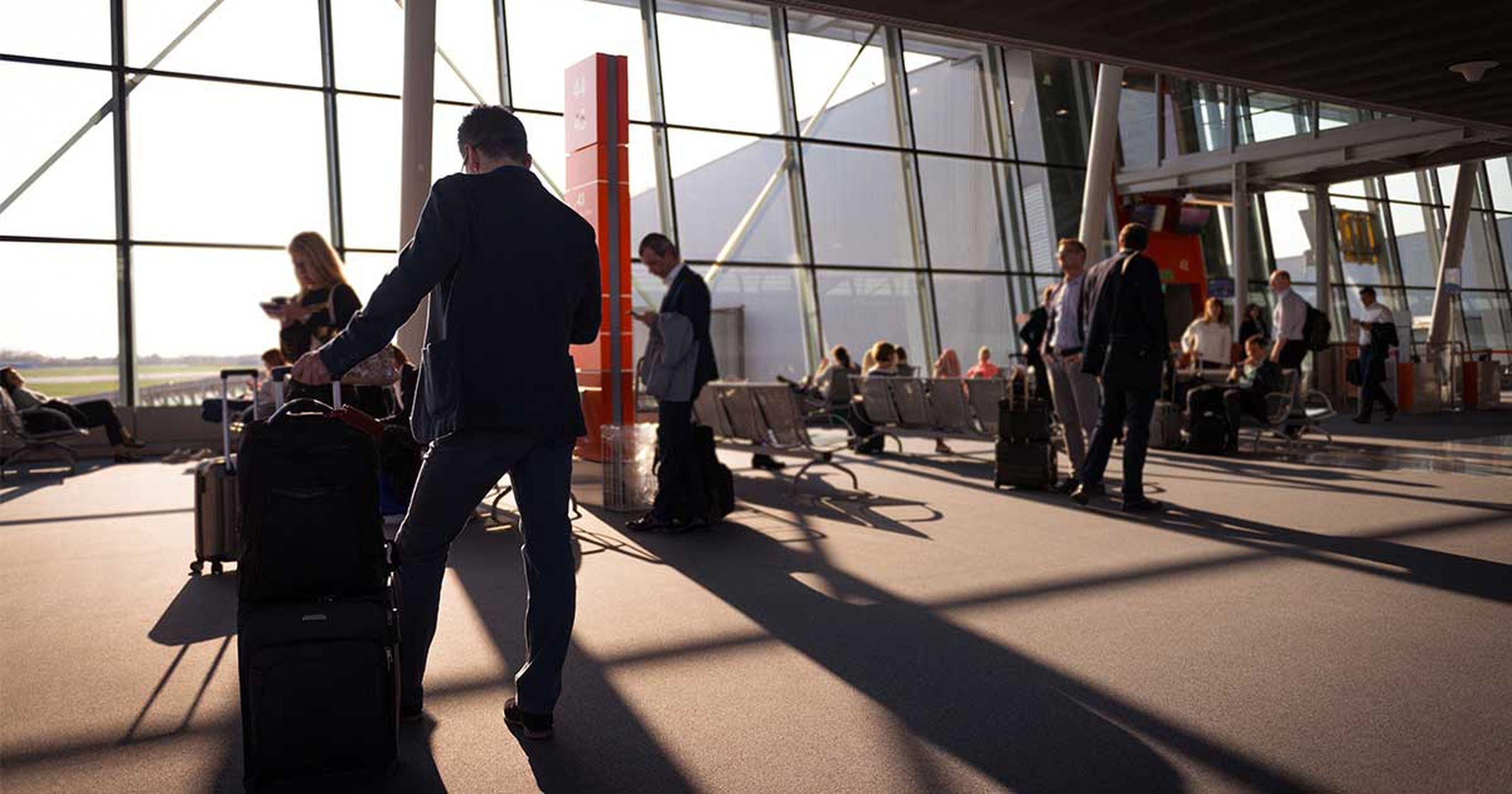 Menschen mit Gepäck in einem modernen Flughafen-Terminal bei Sonnenuntergang, mit großen Fenstern im Hintergrund.