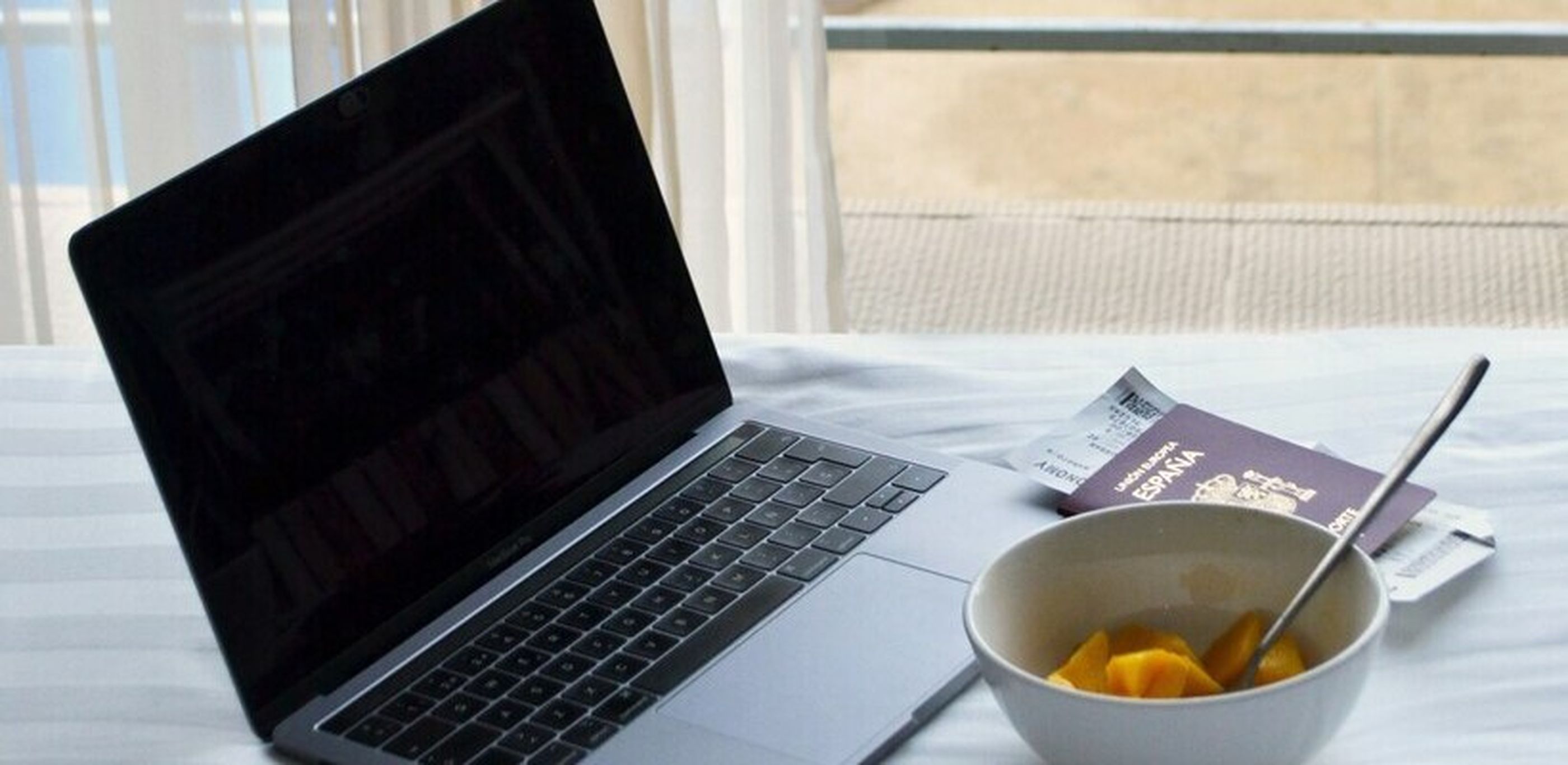 Ein Laptop auf einem  Bett neben einer Obstschale und einem Reisepass