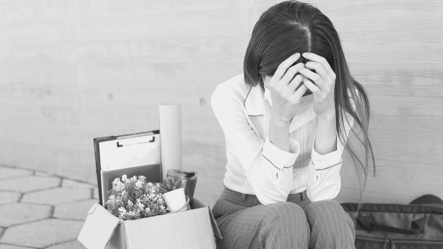 Frau sitzt verzweifelt neben Umzugskarton, Hände an Kopf, Arbeitsverlust, symbolisch für Kündigung und Arbeitslosigkeit.