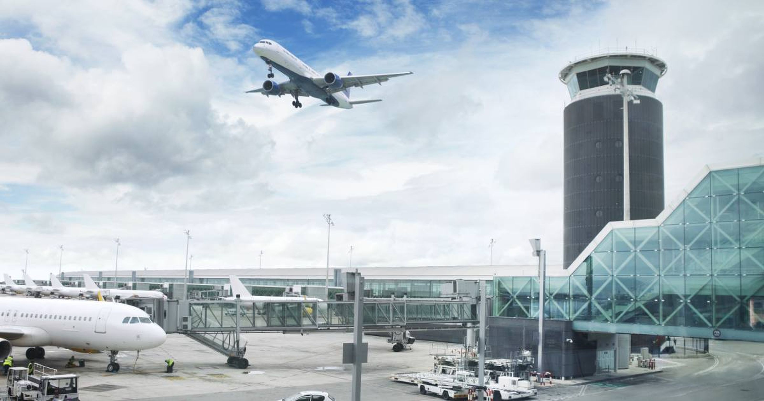 Flugzeug beim Start über Flughafen mit Terminal und Kontrollturm, Wolken am Himmel.