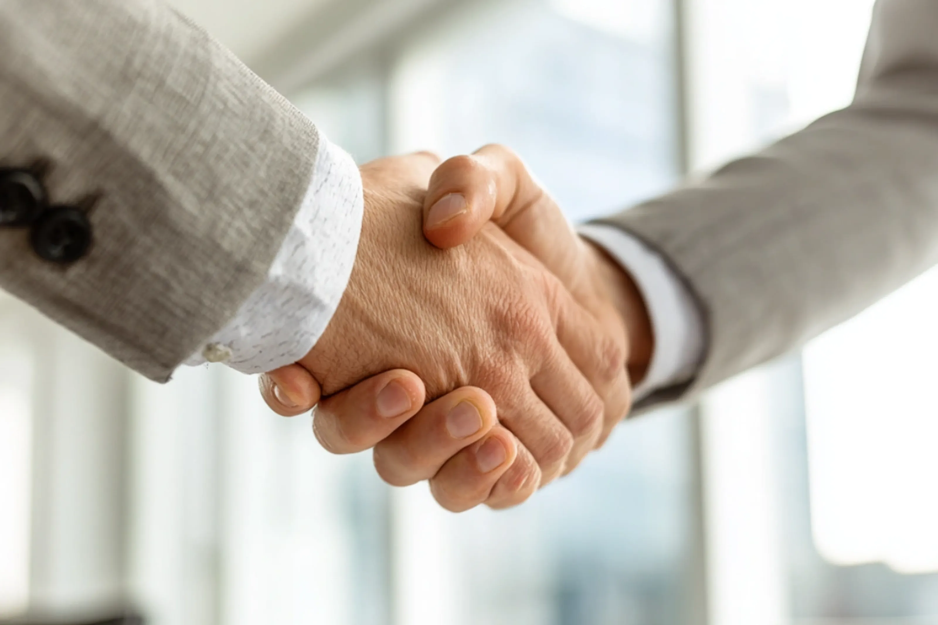 Zwei Personen geben sich die Hand in einem modernen Büro, symbolisiert Geschäftspartnerschaft und Einigung.