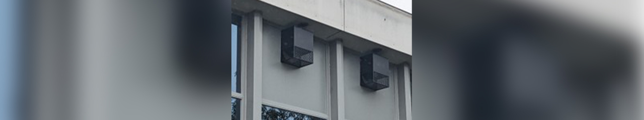 Facade of a building with large windows and two black rectangular boxes mounted on the wall below the roof