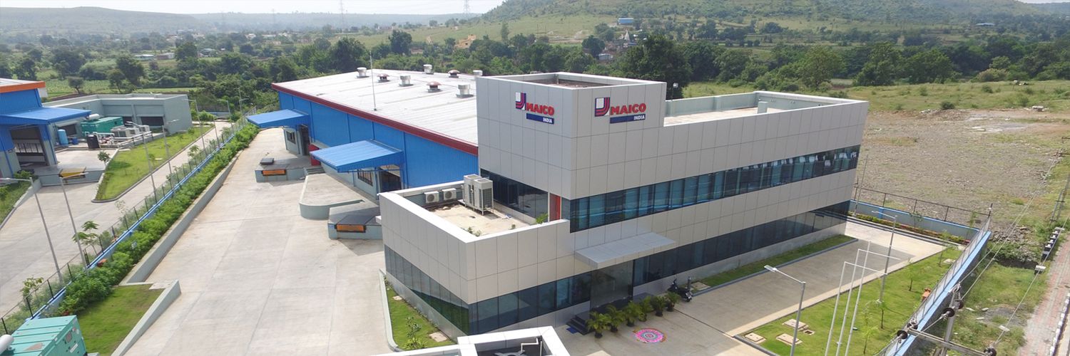 Zweistöckiges Bürogebäude mit MAICO-India-Logo, großen Fenstern und blauen Überdachungen an der Laderampe.