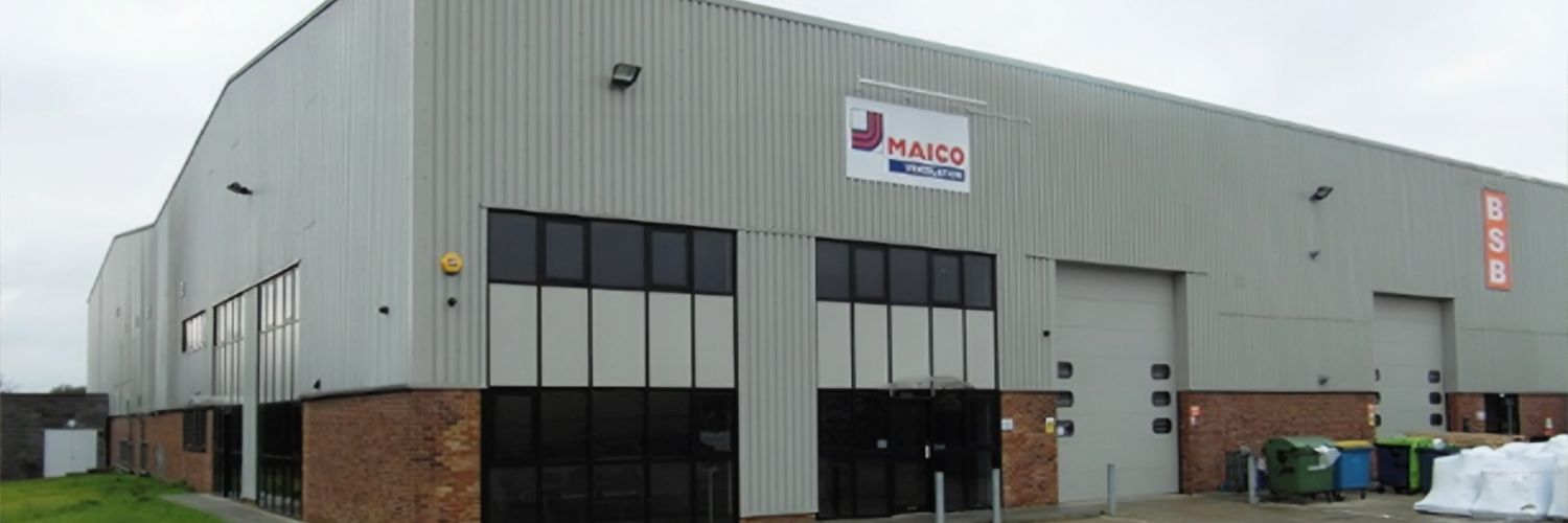 Großes graues Industriegebäude mit mehreren Fenstern und einem Schild mit dem Schriftzug 'MAICO' an der Fassade.