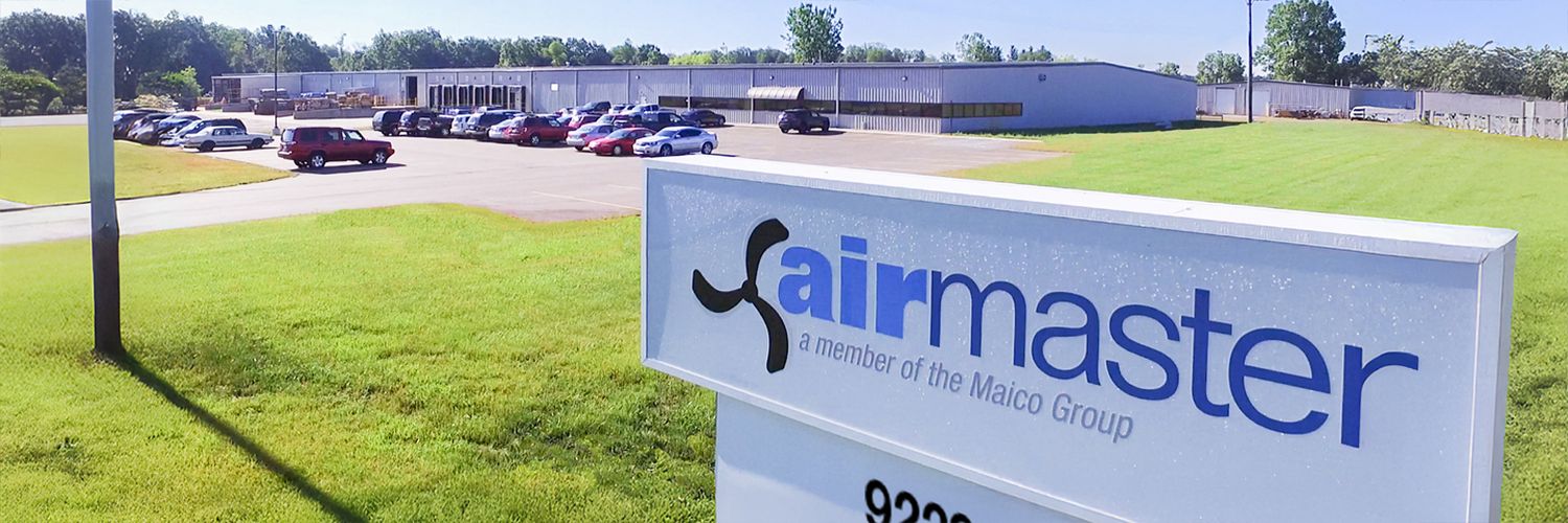 Weitläufiges Firmengelände mit flachem Gebäude im Hintergrund und einem weißen Schild mit Schriftzug airmaster im Vordergrund.