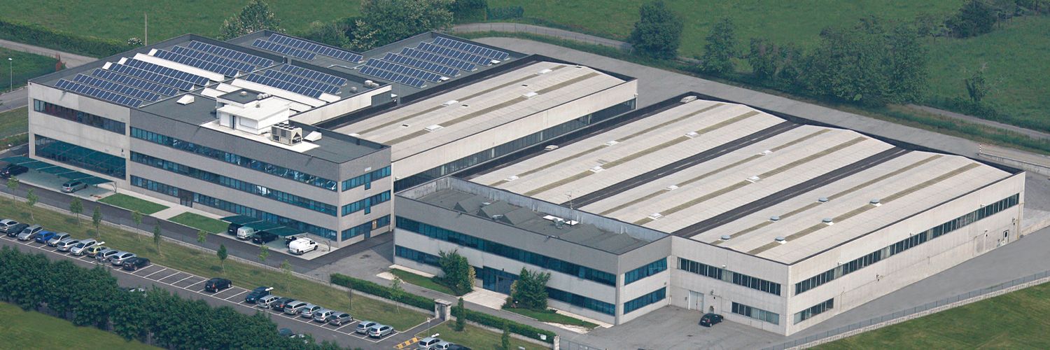 Aerial view of a large industrial complex with multiple connected buildings, parking lots, and surrounding green fields