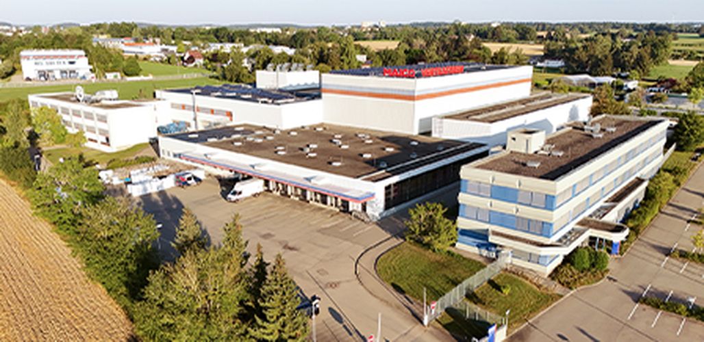 Aerial view of a large industrial complex with several white buildings and the words “MAICO Ventilatoren” on the roof.