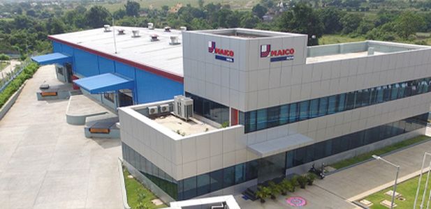 Zweistöckiges Bürogebäude mit MAICO-India-Logo, großen Fenstern und blauen Überdachungen an der Laderampe.