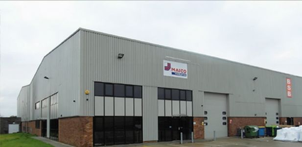Großes graues Industriegebäude mit mehreren Fenstern und einem Schild mit dem Schriftzug 'MAICO' an der Fassade.