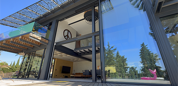 A modern glass façade of a two-storey house, with the interior clearly visible and the reflection of trees in the glass