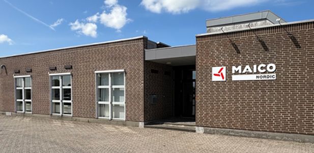 Low brick building with multiple windows and the sign 'MAICO Nordic' on the facade under a blue sky with clouds