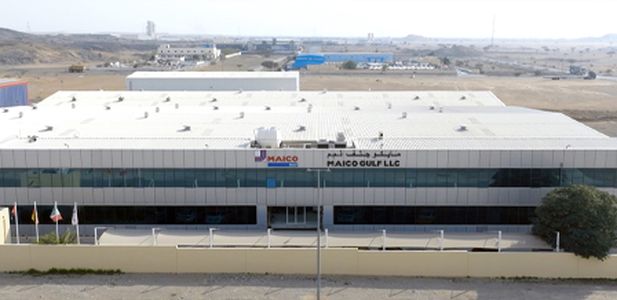 Flaches, rechteckiges Industriegebäude mit weißem Dach und MAICO-Gulf-Logo an der Fassade, umgeben von karger Landschaft.
