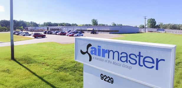 Weitläufiges Firmengelände mit flachem Gebäude im Hintergrund und einem weißen Schild mit Schriftzug airmaster im Vordergrund.
