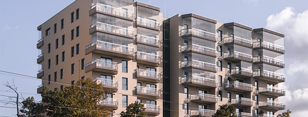 Multi-story residential building with balconies and glass railings against a blue sky