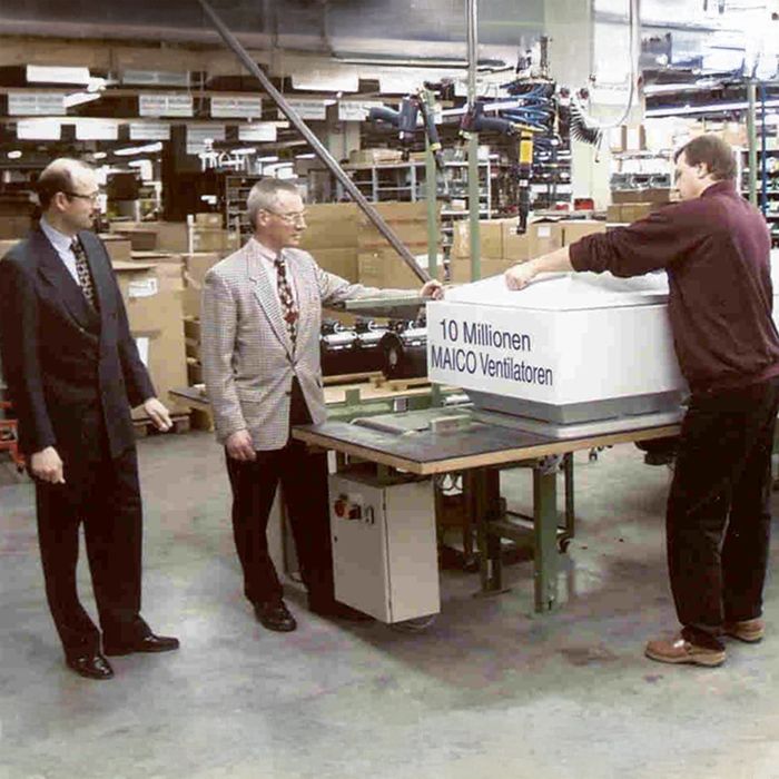 Drei Männer stehen in einer Fabrikhalle auf einem Tisch liegt ein Ventilator mit der Aufschrift „10 Millionen MAICO-Ventilatoren“