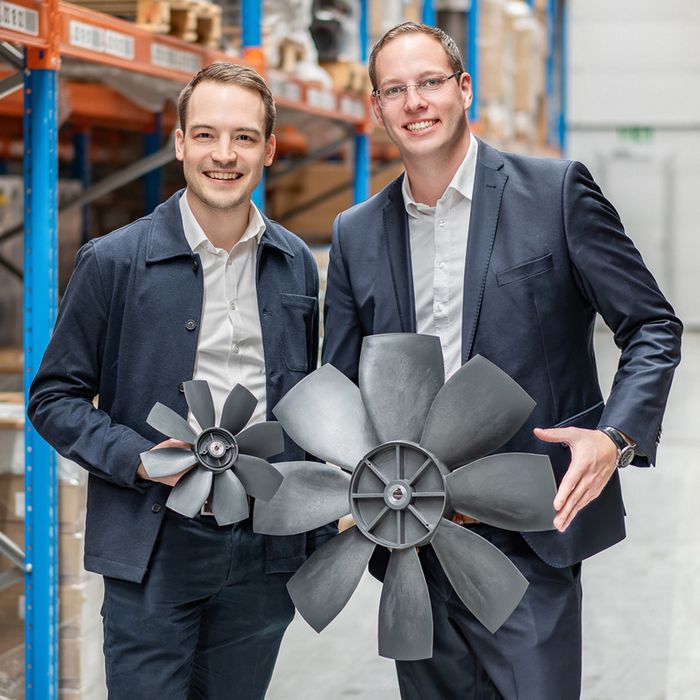 Zwei Männer in Anzügen stehen in einem Lagergang und halten jeweils ein Flügelrad