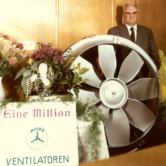 Mann in Anzug steht hinter großem Ventilator mit acht Metallflügeln, davor Schild mit Text 'Eine Million VENTILATOREN'