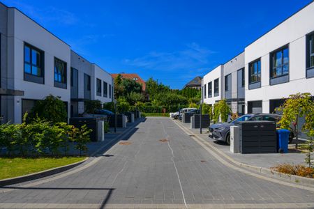 View of a modern residential area with white two-story houses on both sides of a paved street under a blue sky