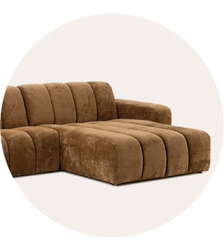 Bruine, zachte hoekbank met een brede chaise longue en afgeronde kussens met verticale stiknaden tegen een lichte, neutrale achtergrond.