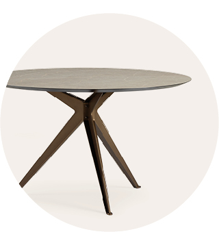 Ronde moderne tafel met een slank grijs blad en hoekige bronzen metalen poten tegen een lichte achtergrond.