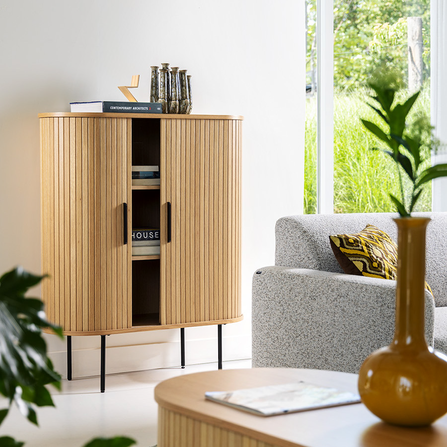 Woonkamer in Scandinavische stijl met een geribbelde houten kast op zwarte poten naast een grijze bank, planten en een mosterdgele vaas op een lage tafel.