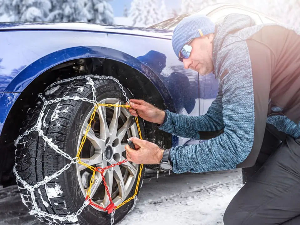 Mann montiert Schneeketten an Auto