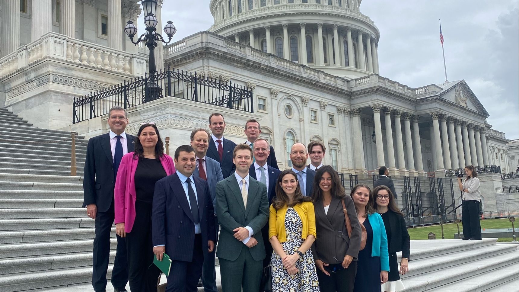 A group of people standing on the steps outside the US Capitol building under a cloudy sky.