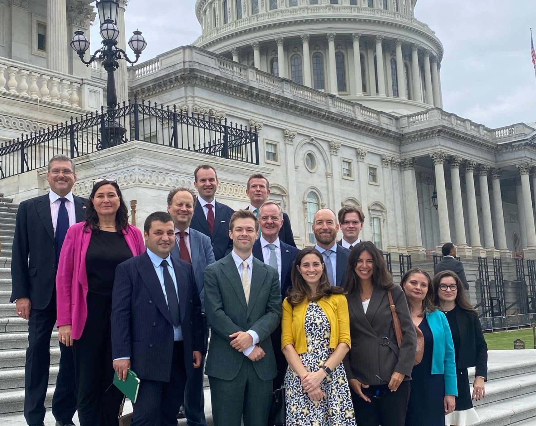 A group of people standing on the steps outside the US Capitol building under a cloudy sky.