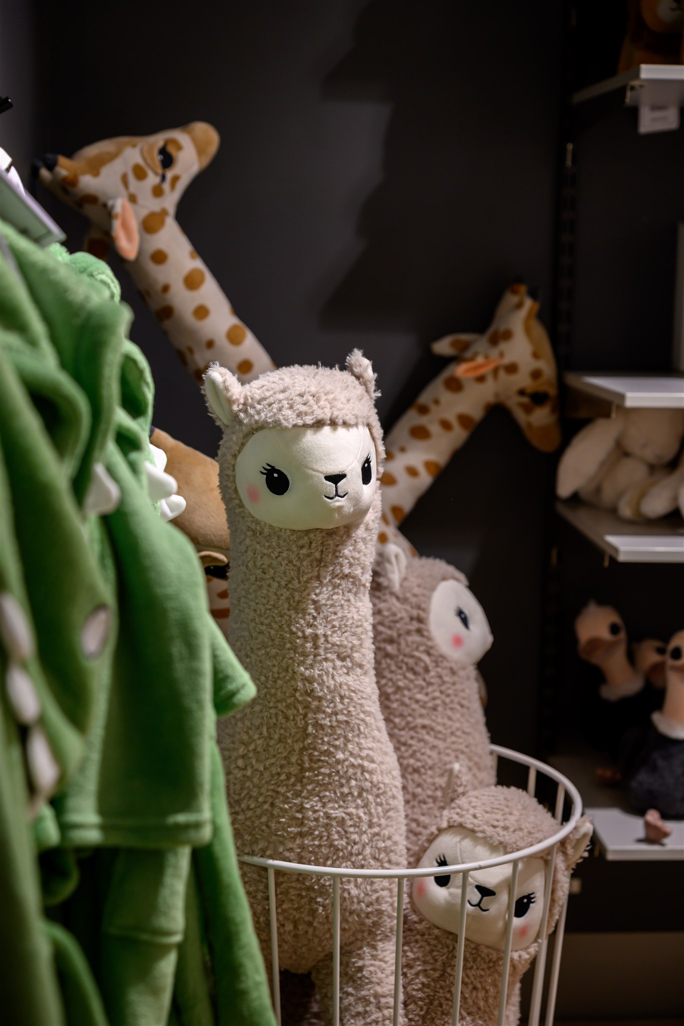 Plush alpacas and giraffes in a store display, with a green dinosaur-themed garment hanging nearby.