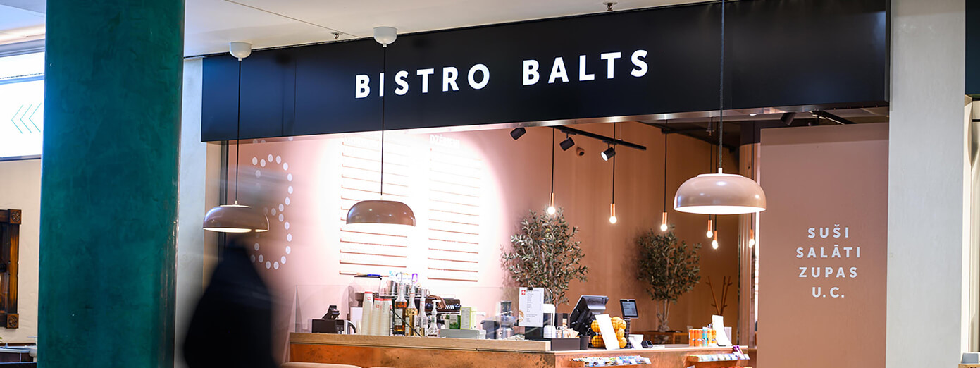 Modern bistro counter with "Bistro Balts" sign, warm lighting, hanging lamps, and menu items like sushi and salads displayed.