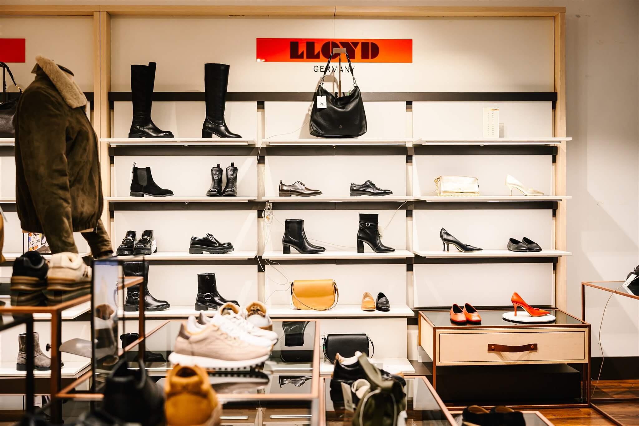 Shoe store display with various styles of footwear, including boots, heels, and sneakers, arranged on shelves and tables.