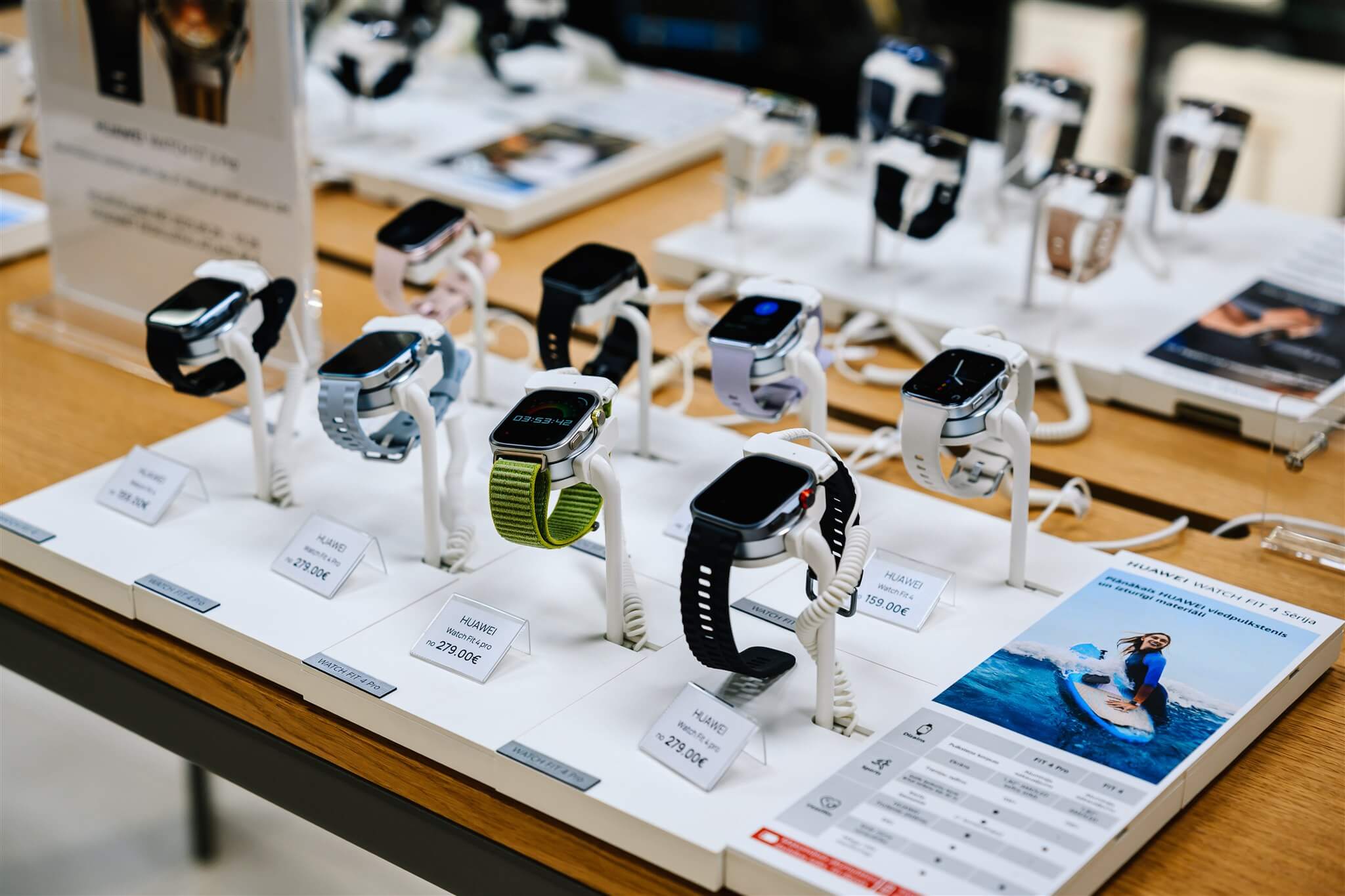 A display of various smartwatches on stands, featuring different designs and colors, with price tags on a wooden table in a store.