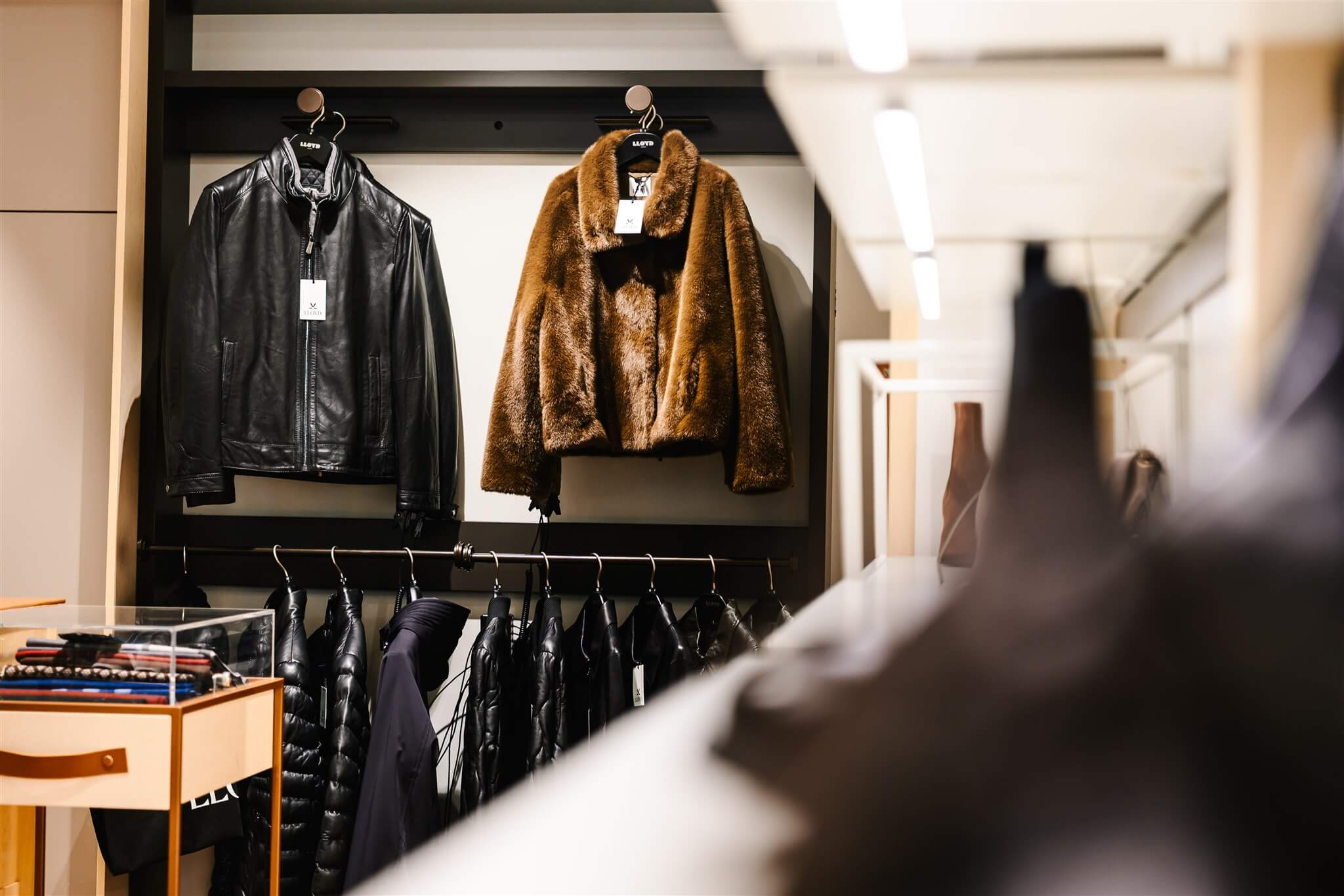 Leather and fur jackets hanging on a rack in a clothing store, with more jackets displayed below.