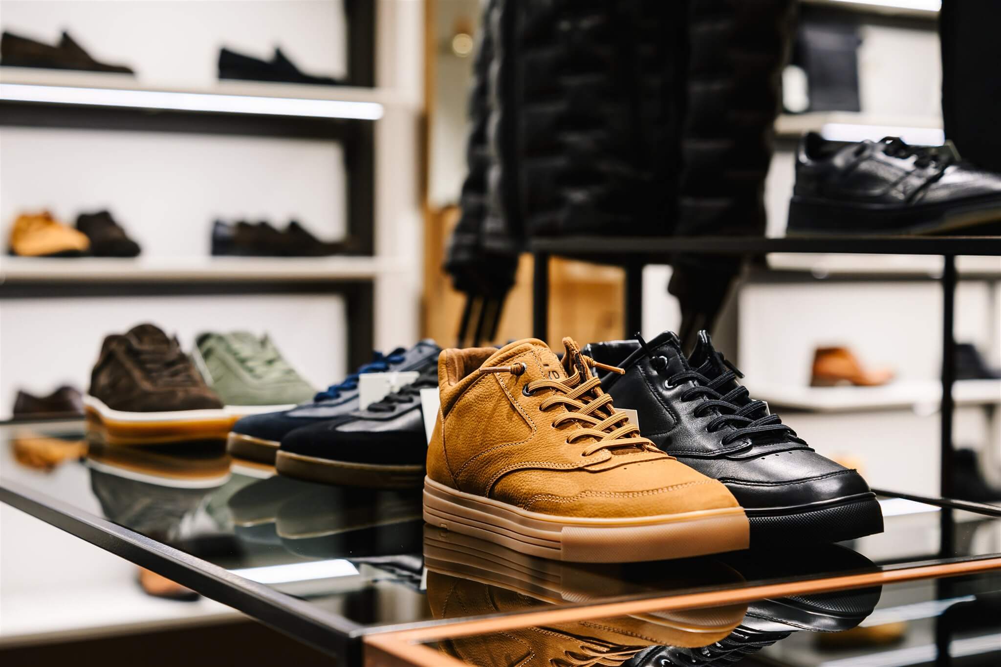 A display of various sneakers on glass shelves, featuring brown and black pairs prominently in the foreground, with more shoes in the background.