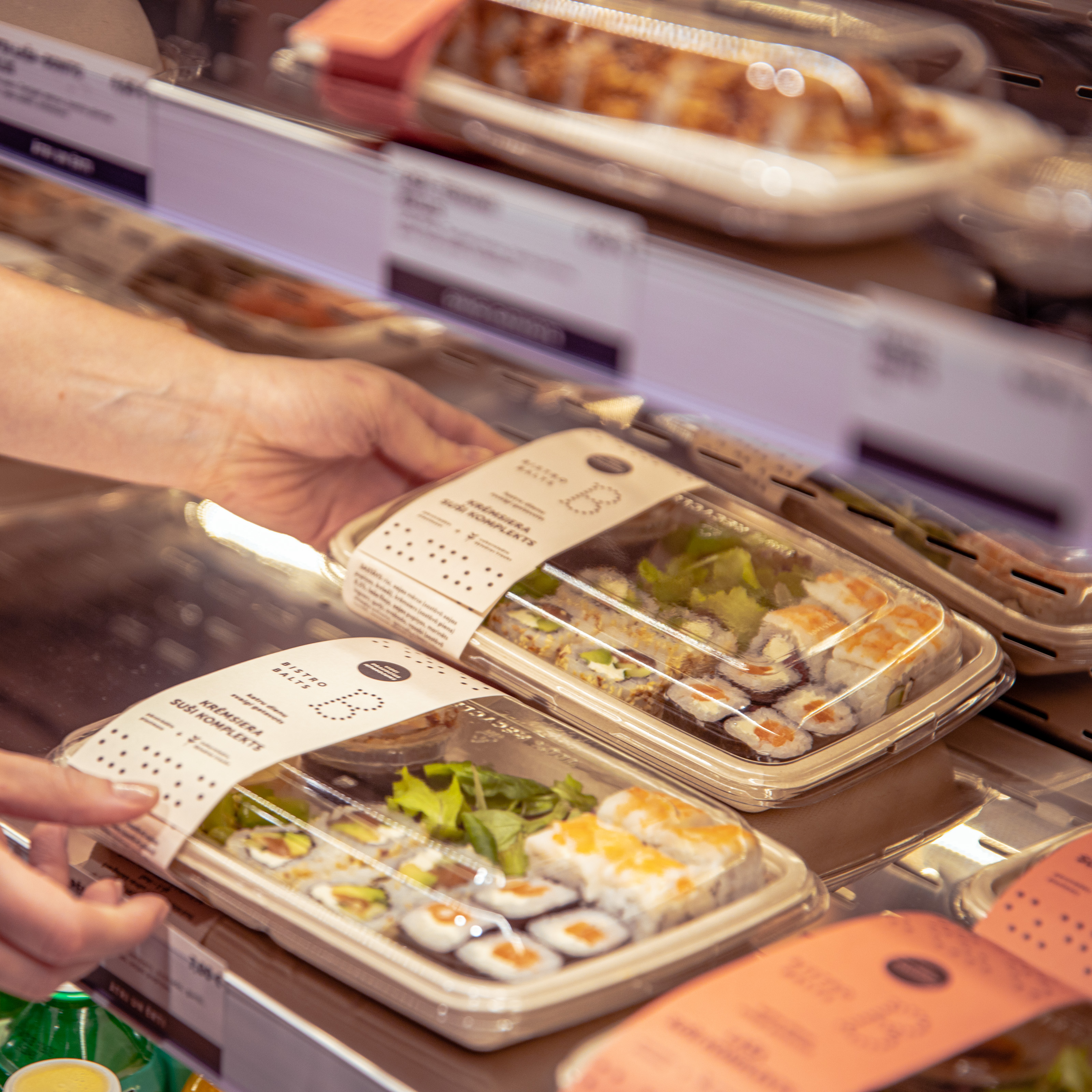 Person selecting packaged sushi from a refrigerated display in a store.