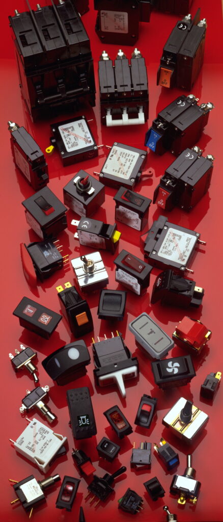 Various electrical switches and circuit breakers are scattered on a red surface, showcasing different sizes and designs.