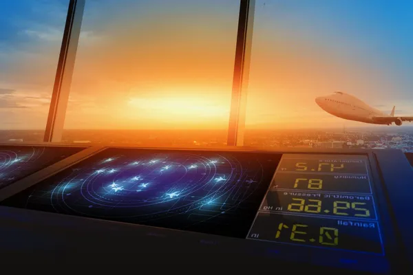 Air traffic control tower with radar screens, overlooking a sunset sky as a plane takes off in the distance.
