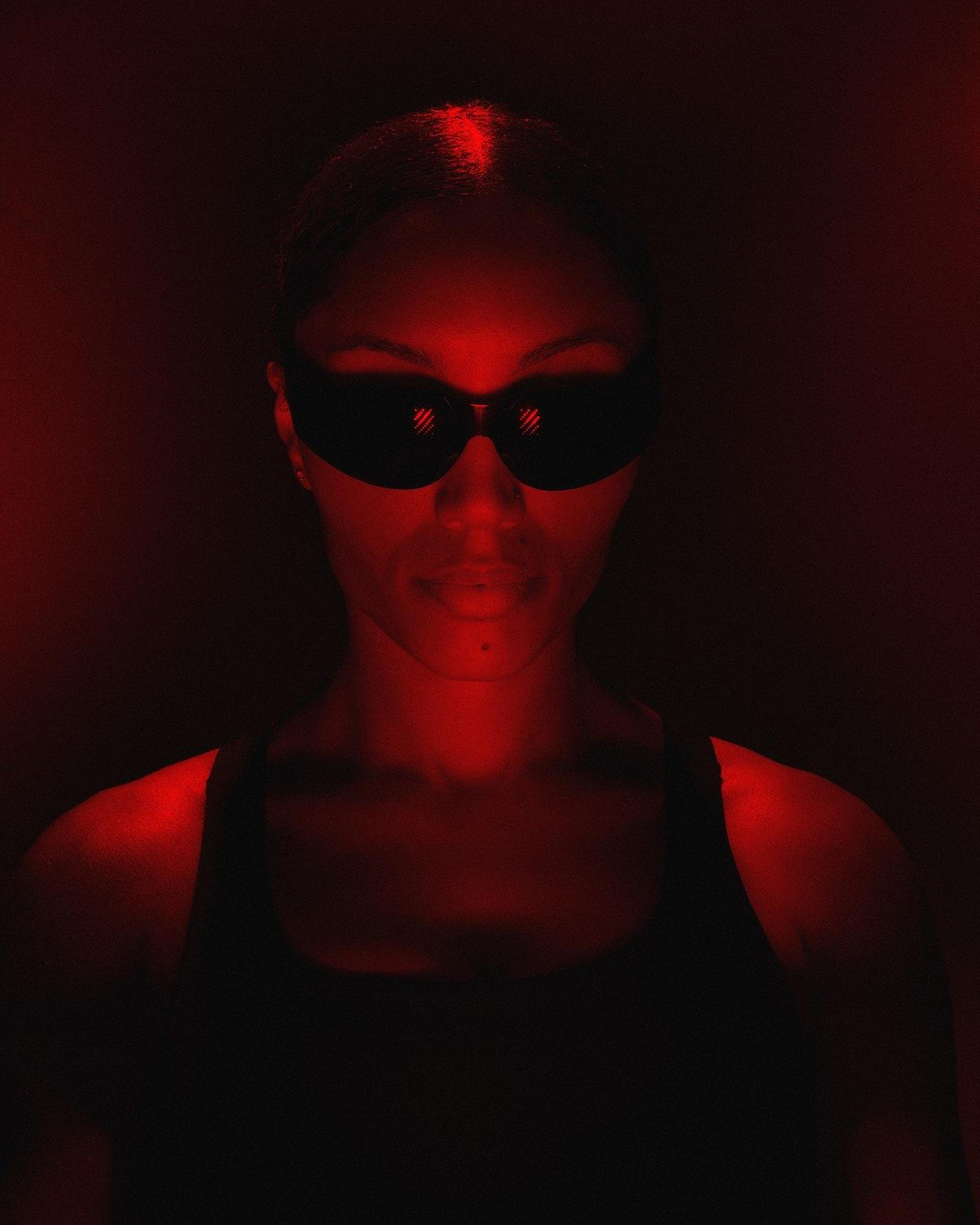 A woman in dark sunglasses lit by red light.