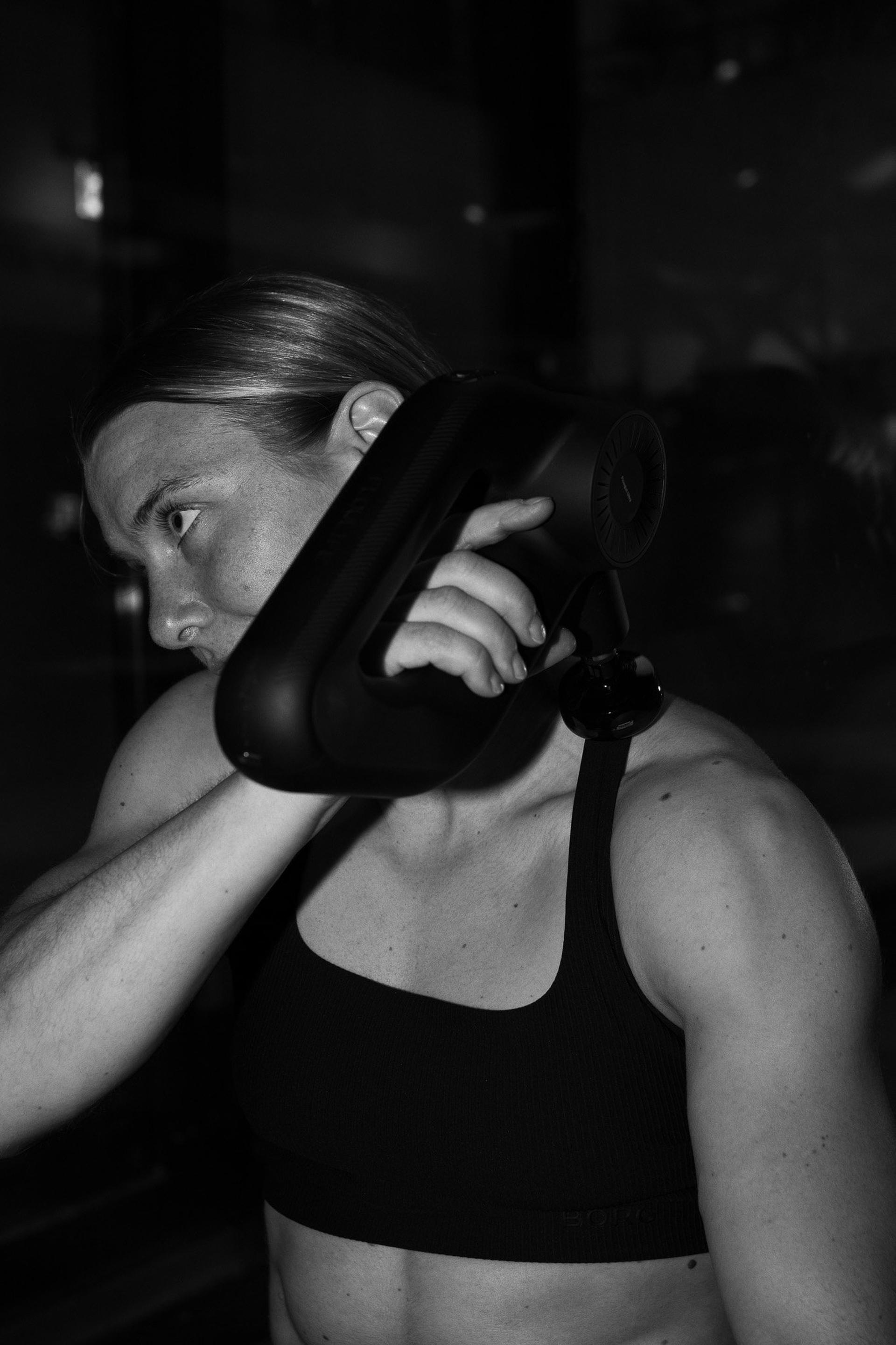 Athlete using a massage gun on her shoulder