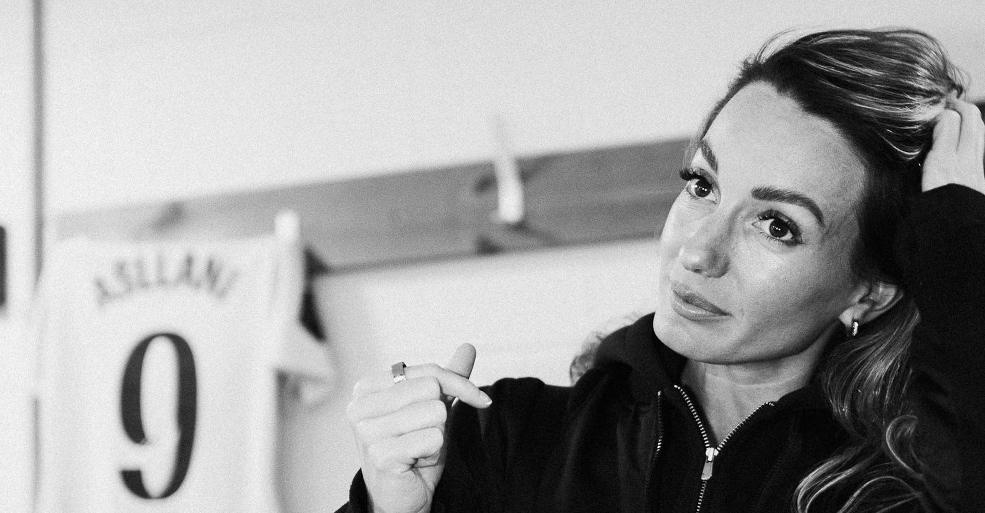 Black and white portrait of a footballer in a changing room, her number 9 shirt hanging behind her