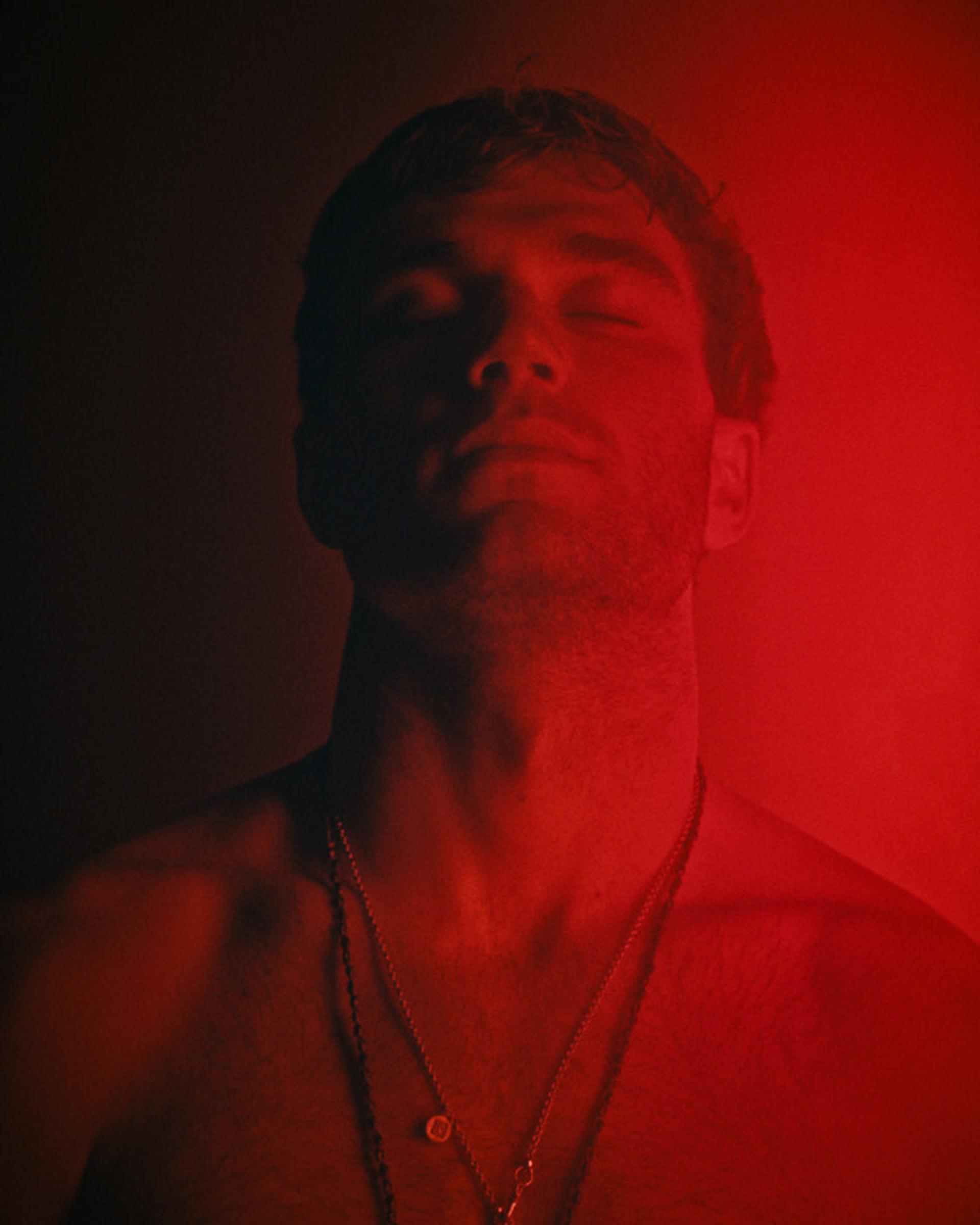 Close-up of Jack Draper with his eyes closed, lit by red light.