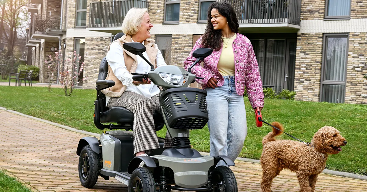 Vrouw op scootmobiel lacht naar haar kleindochter. Samen laten ze een hond uit