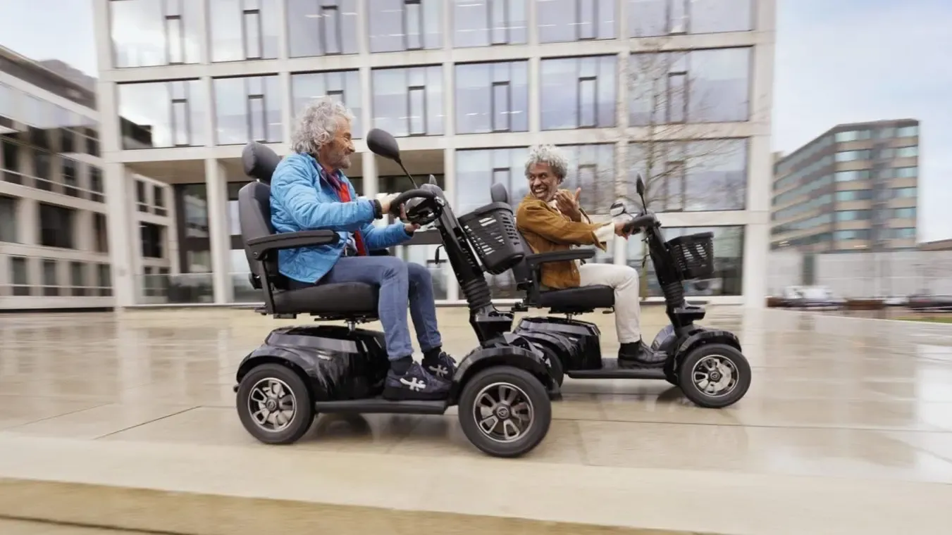 Twee mensen rijden met hun scootmobiel over een plein