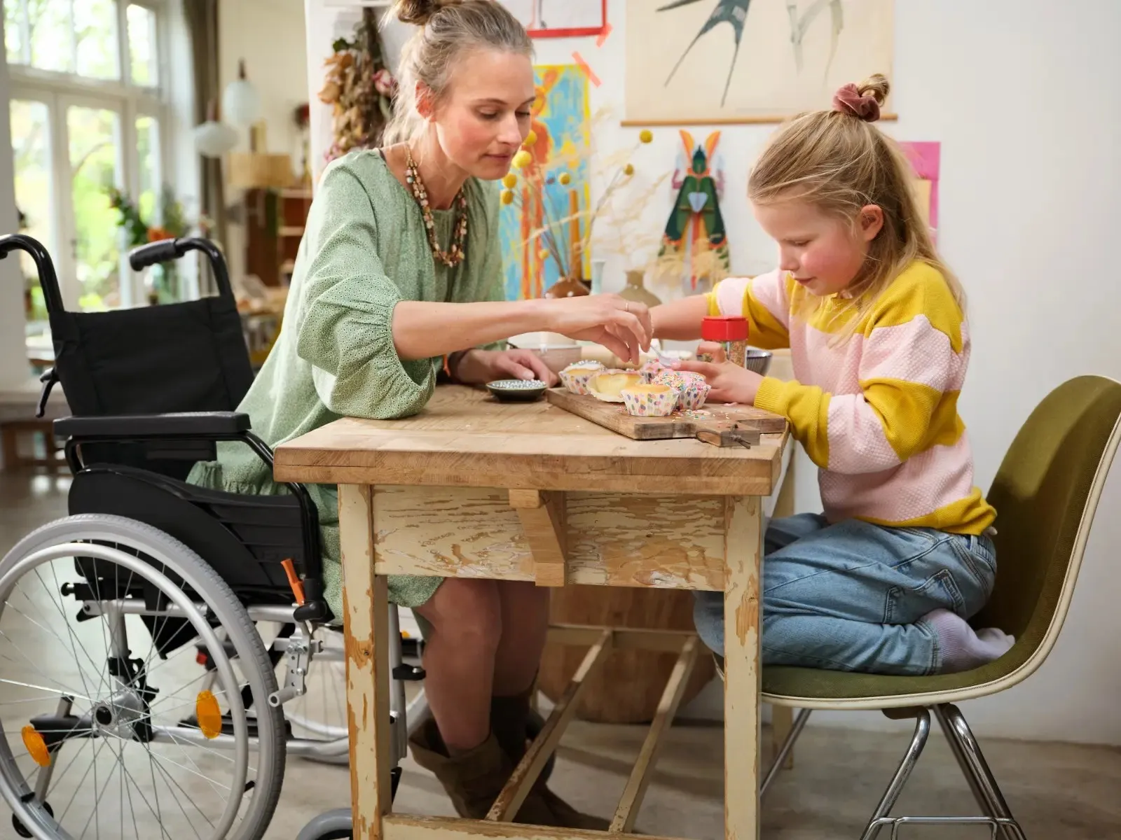 Vrouw in rolstoel met kind aan tafel die cupcakes maakt