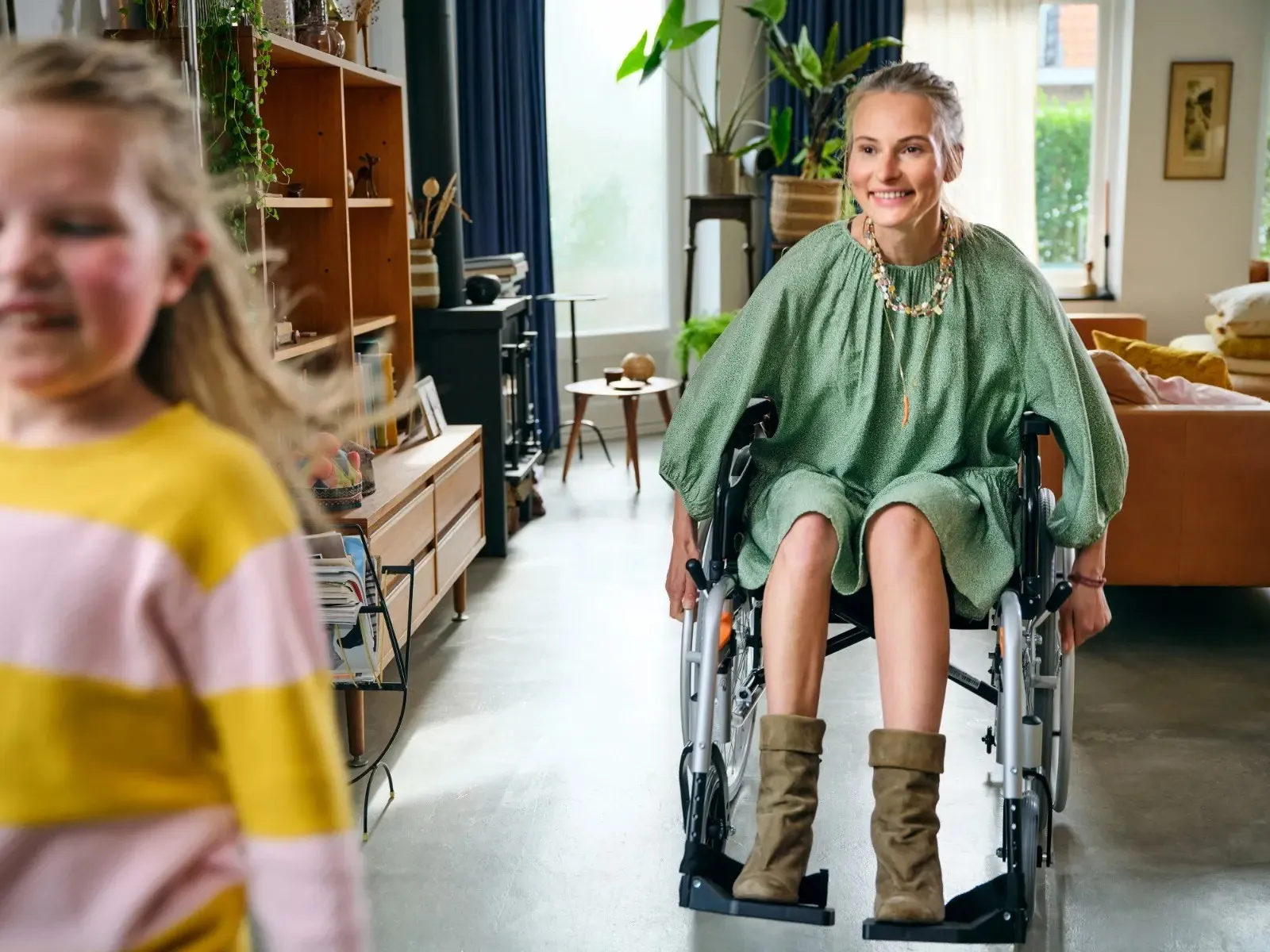 Vrolijke vrouw rolt achter dochter aan in de rolstoel door het huis