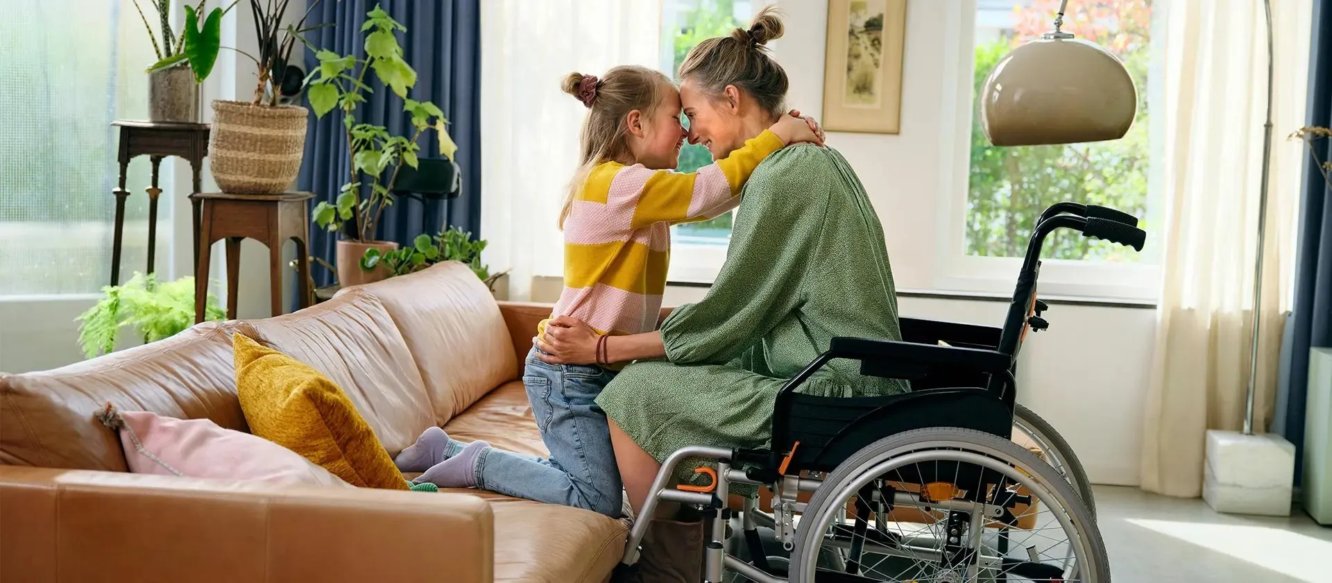 Eindgebruiker in rolstoel met een kind die met de knieën op de bank zit en de moeder omhelst