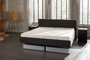 Modern verstelbaar bed in een stijlvolle slaapkamer met grote ramen, jaloeziegordijnen en eigentijdse inrichting.