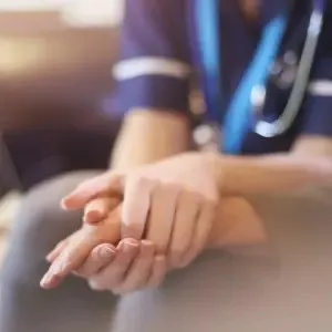 Verplegend persoon houdt hand vast van eindgebruiker met focus op de handen